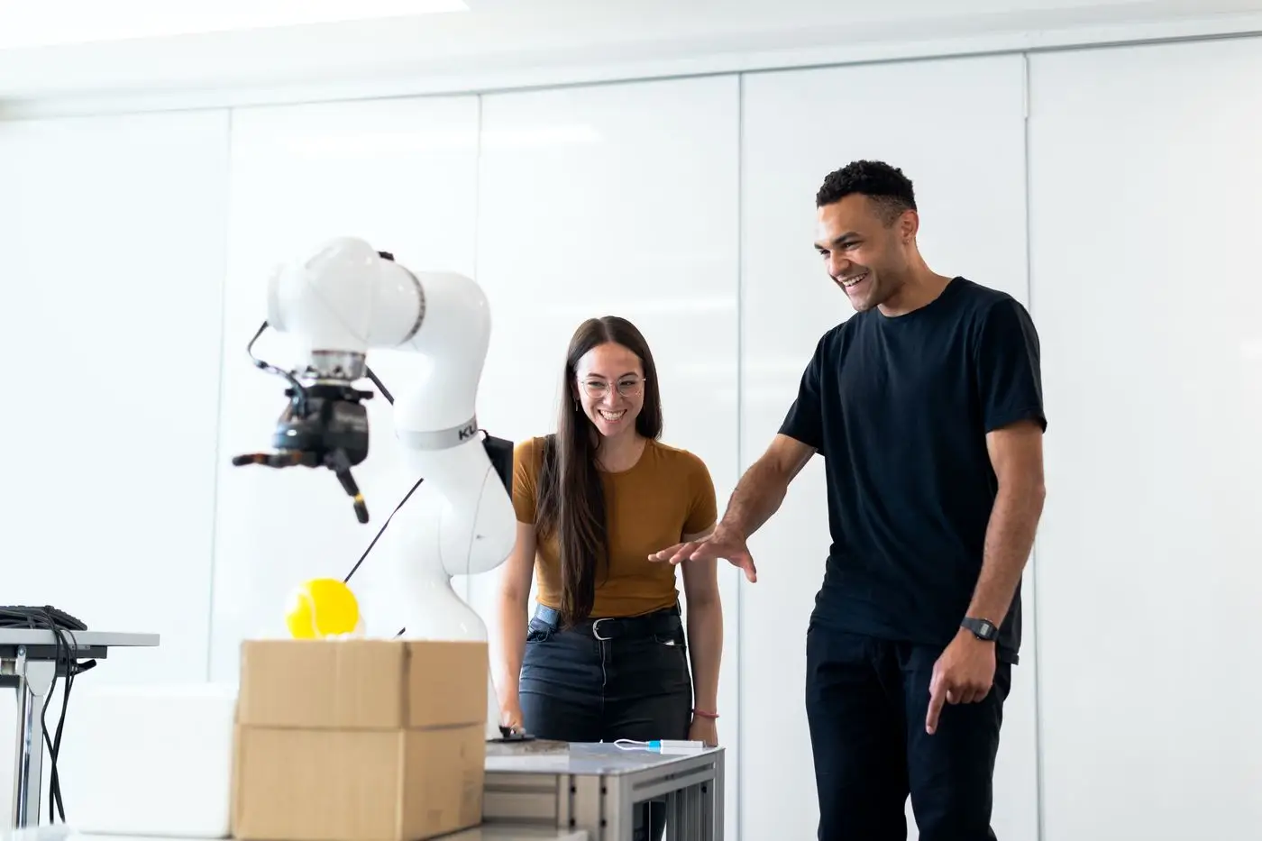 Two engineers working alongside a white industrial robotic arm in a bright laboratory